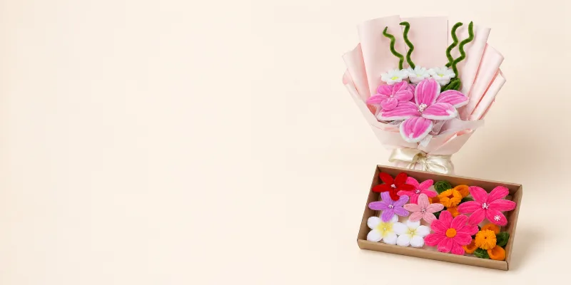 A LEAP bloom box, wrapped bouquet and two flower keychains arranged together on cream silk with a printed card