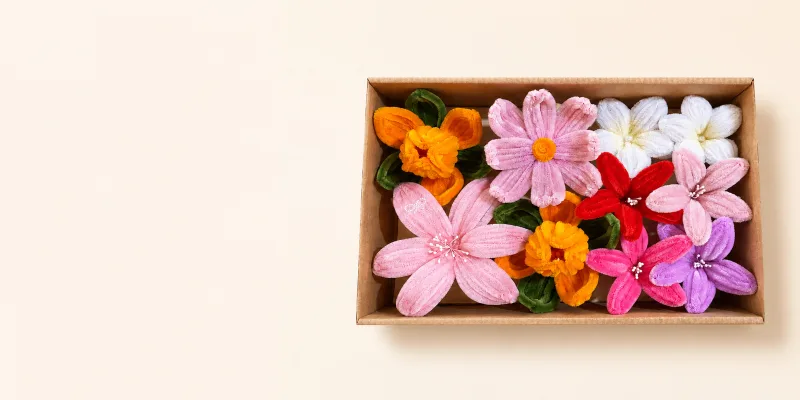 A kraft box of handmade chenille blooms in pink, red, orange and white, beside a printed LEAP card